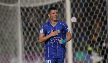 یاسر آسانی با پیراهن استقلال در حال ترکاندن یک بادکنک کاملاً قرمز است