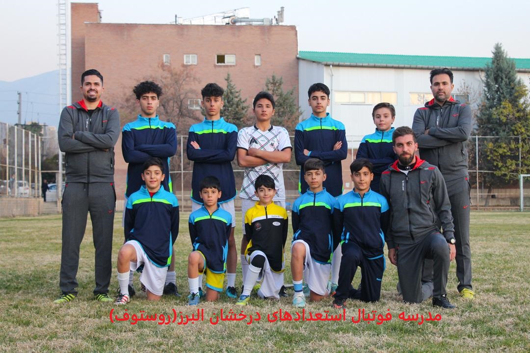 عکس تیمی بازیکنان فوتبال نونهالان در زمین چمن با گرمکن های سورمه ای به همراه مربیان خود